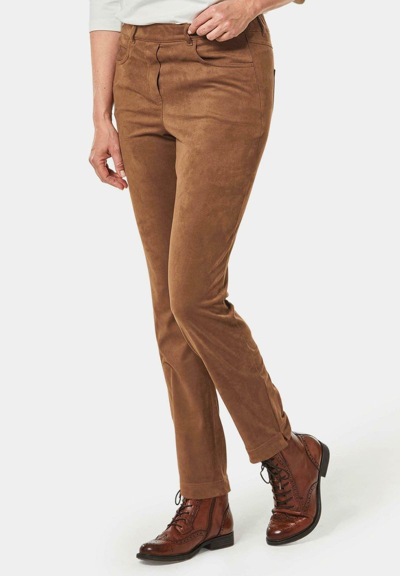 Pantalons en daim marron avec une coupe slim, dotés d'une fermeture éclair, de poches avant et de détails de couture. Associés à des bottines à lacets marron.