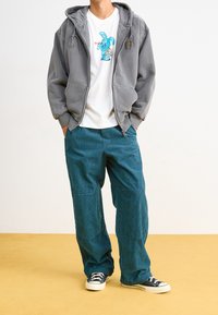 Gray zip-up hoodie with a kangaroo pocket, paired with teal corduroy pants and black sneakers. White t-shirt features a colorful rabbit graphic.