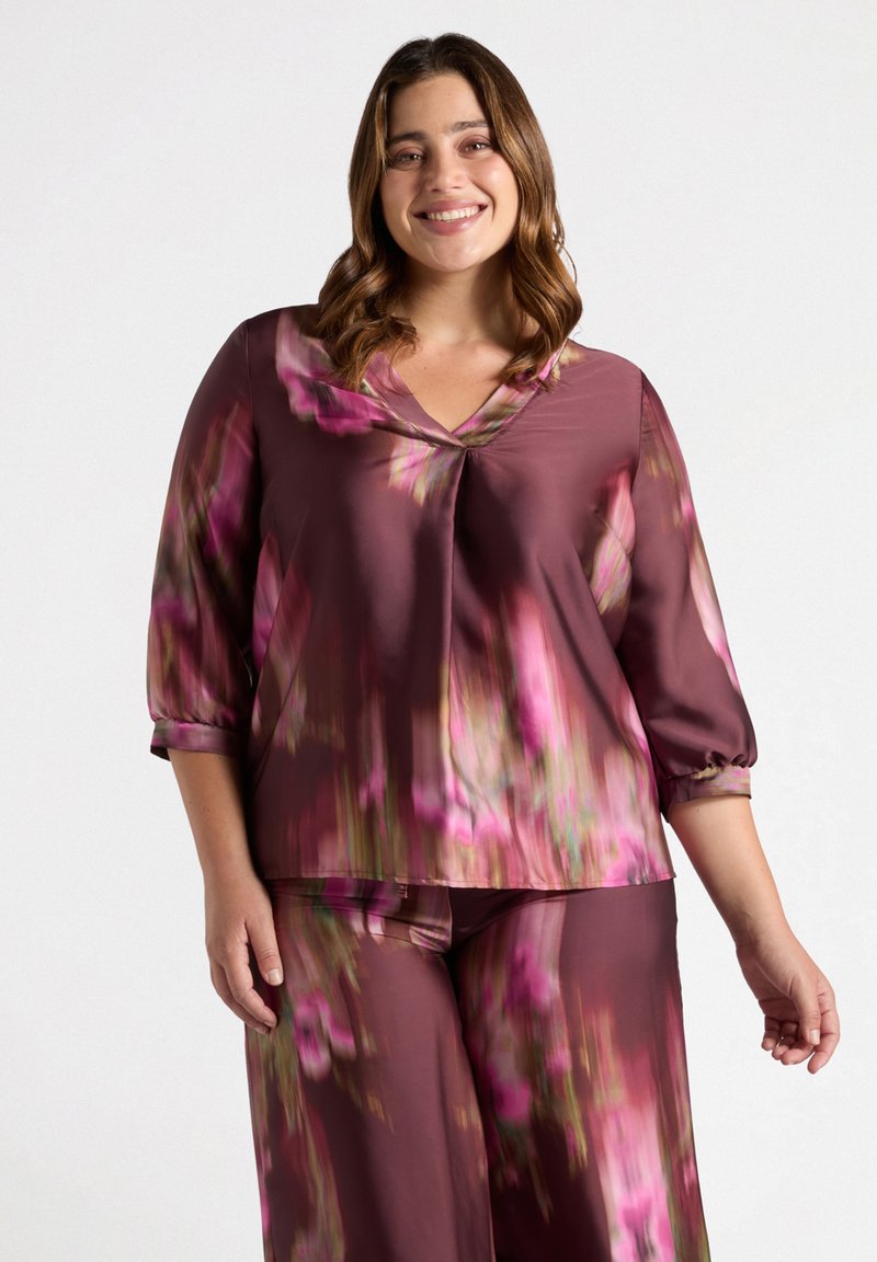 Blusa a maniche lunghe, con scollo a V in satin bordeaux profondo con motivi floreali in rosa e verde. Presenta una vestibilità rilassata e maniche con polsini.