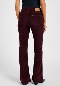 Burgundy corduroy flared pants with a leather logo patch at the back waistband and double pockets, featuring a smooth texture.