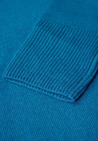 Tissu de pull turquoise avec une texture en côtes ; présente un poignet replié, mettant en avant sa douceur et un motif de couleur unie.