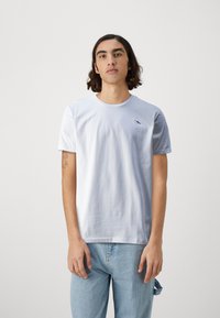 Tricou din bumbac de culoare albastră deschisă, cu mâneci scurte, guler rotund și un mic design brodat cu un păsărele pe pieptul stâng. Blugi din denim deschis.