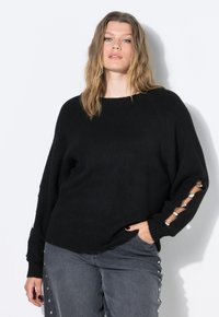 Czarny dzianinowy sweter o luźnym kroju i długich rękawach z metalicznymi akcentami na mankietach. W połączeniu z szarymi dżinsami z bocznymi ćwiekami.