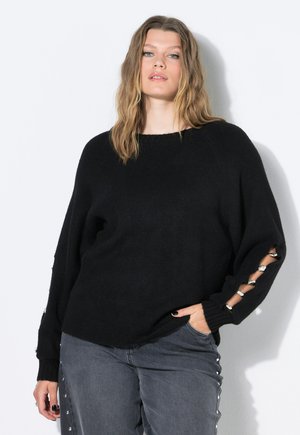 Maglione nero in maglia con vestibilità ampia e maniche lunghe, dotato di accenti metallici nei polsini. Abbinato a jeans grigi con borchie laterali.