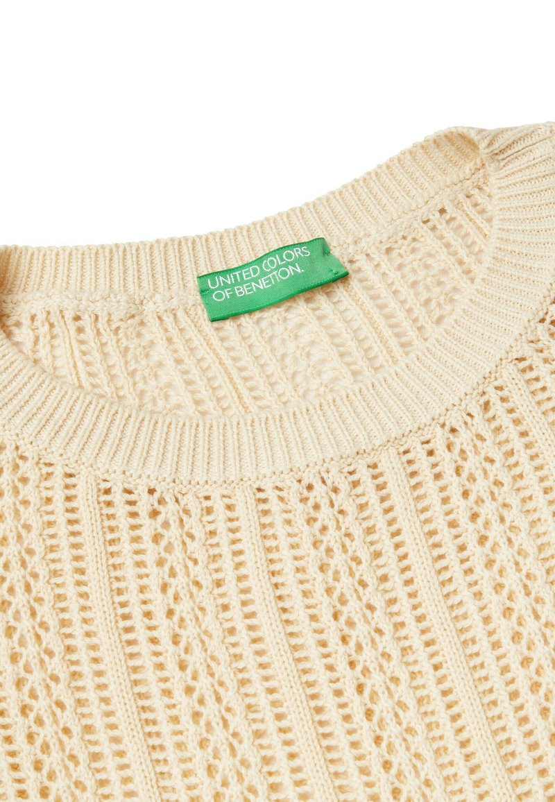 Sweter dziany w jasnym beżu, z teksturowanym wzorem ażurowym. Okrągły dekolt i zielona metka z napisem "United Colors of Benetton."