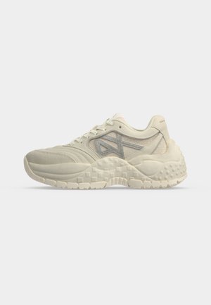 Baskets de sport beiges et grises avec semelle texturée, design à lacets et col rembourré, montrées de profil sur fond blanc.