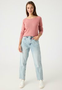 Suéter de punto rosa con un escote amplio, combinado con jeans de talle alto azul claro. Zapatillas blancas completan el atuendo.