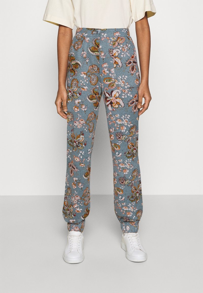 Siniset kukalliset verkkarit, joissa on paisley-kuvio pinkeillä ja vihreillä yksityiskohdilla, joustavat hihansuut ja naru vyötäröllä, yhdistettynä valkoisiin lenkkareihin.