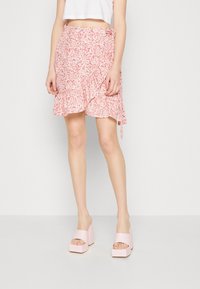 Falda envolvente floral de color rosa con dobladillo con volantes y detalle de lazo, combinada con zapatos de plataforma rosa gruesos que muestran los dedos de los pies. Textura de tela suave.