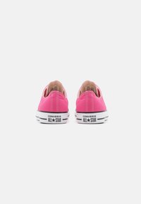 Converse sneakers in bright pink canvas with white rubber soles. Features black accents with "ALL STAR" printed on the heel. Classic low-top design.
