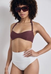Bikini-Top in Kastanienbraun mit geripptem Textur und Halterneck; hochgeschnittene Bikinihose in Weiß mit glatter Oberfläche und minimaler Detailgestaltung.