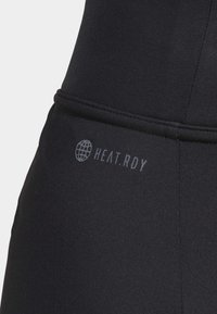 Sort atletisk stof med glat tekstur, præget af "HEAT.RDY" logo i grå. Designet har en tætsiddende form og minimalistiske sømme.