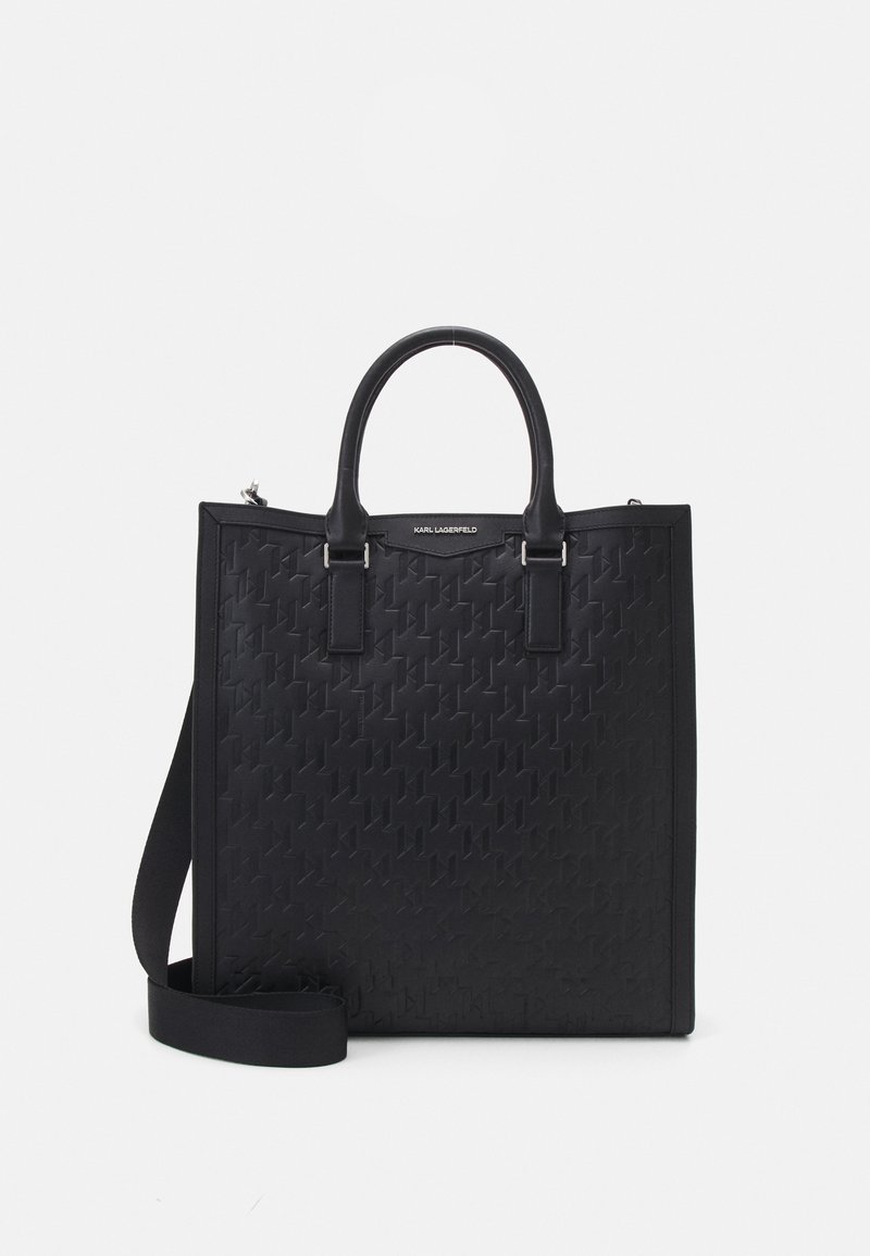 Sac fourre-tout noir présentant un motif tissé, une texture lisse, deux poignées et une bandoulière réglable. Accents en métal argenté visibles.