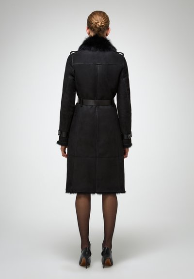 Musta shetlankotteri turkiskauluksella, vyöllä varustettu vyötärö ja hihansuut. Ominaisuuksiin kuuluu puolipitkä muotoilu ja teksturoitu viimeistely helmaosassa.