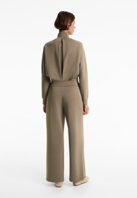 Completo due pezzi beige a coste che presenta un top con colletto alto e schiena drappeggiata, accompagnato da pantaloni a gamba larga, realizzato in un morbido tessuto testurizzato.