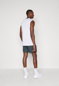 Witte mouwloze tanktop, donkergroene shorts, witte sneakers en witte sokken. Glad materiaal, comfortabele pasvorm en minimale ontwerpdetails.