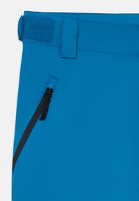 Vêtement bleu avec une poche zippée noire en angle et un onglet de taille réglable en Velcro sur une surface en tissu lisse.