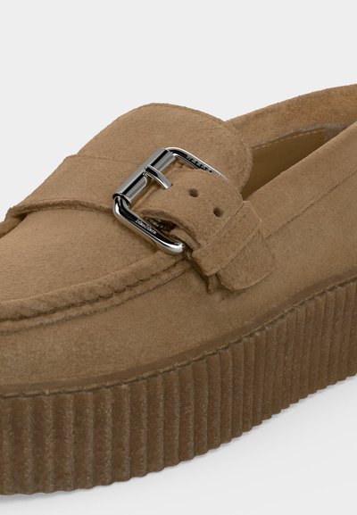 Mocassin plateforme en daim marron clair avec semelle épaisse rainurée et boucle carrée argentée sur la bride supérieure.