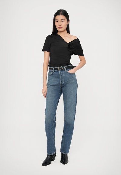 Juodas viršus be petnešėlių, pagamintas iš tekstūruotos medžiagos su gėlėta puošmena, derinamas su aukšto liemens mėlynais džinsais ir juodais aulinukais.