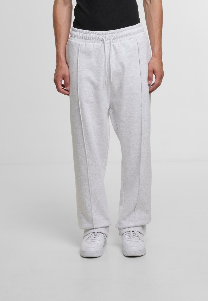 Light gray sweatpants with a drawstring waistband, side pockets, and a relaxed fit, paired with white sneakers on a neutral background.