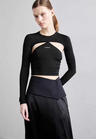 Black long-sleeve crop top with cut-out details and logo; paired with a black pinstripe skirt featuring a folded waist design.