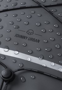 Vízálló szürke hátizsák felülete kiemelkedő vízcseppekkel, fehér csíkkal és fekete zsinórokkal, amelyen a "JOHNNY URBAN" felirat található.