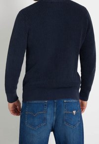 Marinblå räfflad stickad tröja med långa ärmar, i kombination med blå jeans som har bakfickor och kontrasterande sömmar.