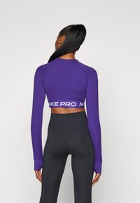 Lilla langermet crop topp med en tettsittende passform og Nike Pro-merke på den elastiske kanten, samt høyhalsede svarte tights.