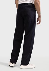 Jeans de culoare albastru închis, cu croială largă și talie înaltă, având două buzunare spate și o textură subtilă. Asortați cu adidași albi.