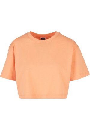Mujer con una camiseta naranja holgada, corta y de manga corta combinada con vaqueros negros de talle alto sobre un fondo liso.