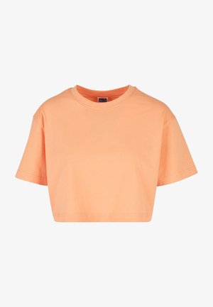 Kobieta nosząca luźny, krótki, pomarańczowy krótki t-shirt w połączeniu z czarnymi, wysokim stanem jeansami na jednolitym tle.