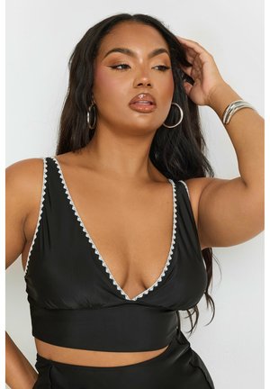 Top cropped noir avec un décolleté en V plongeant, bordure festonnée blanche et bretelles réglables. Tissu lisse avec un design ajusté.