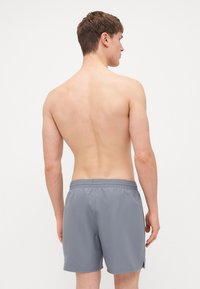 Shorts de bain pour hommes en gris clair. Taille élastique avec cordon de serrage. Texture lisse, longueur au-dessus du genou, avec fentes latérales pour une liberté de mouvement.