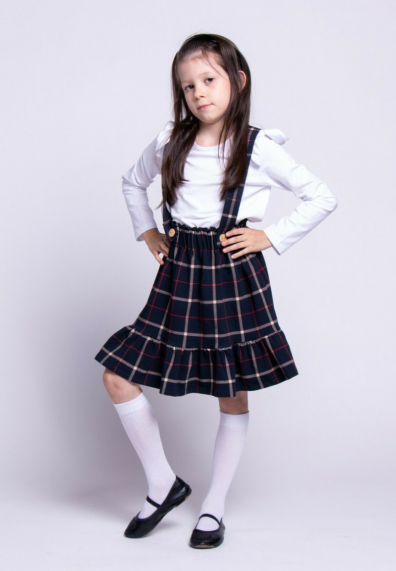 Granatowa sukienka w kratę z rozkloszowanym dołem, regulowanymi ramiączkami i drewnianymi guzikami. Do tego biała koszula z długim rękawem oraz białe skarpetki do kolan.