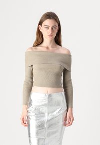 Beige ribbet off-shoulder topp med lange ermer og en kort silhuett. Kombinert med et skinnende sølv blyantskjørt.