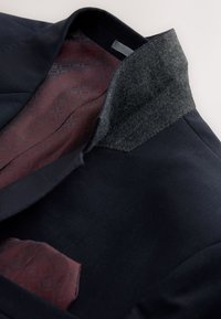 Veste bleu marine avec col en feutre gris foncé, doublure bordeaux à motifs et pochette assortie à l'intérieur.