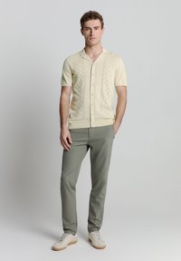 Korte mouw gebreide polo in lichtgeel met een gestructureerd ruitpatroon, gecombineerd met olijfgroene op maat gemaakte broek en lichte sneakers.