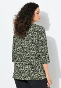 Schwarzes Oberteil mit Blumenmuster und Dreiviertelärmeln, mit lockerem Schnitt und rundem Ausschnitt, kombiniert mit dunklen Jeans.