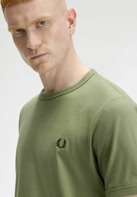 T-shirt in cotone verde oliva con scollatura rotonda, maniche corte e un piccolo logo ricamato sul petto con un design di alloro.