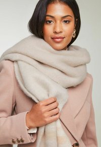 Beige uldhalstørklæde svunget om en pink frakke, med blød tekstur og subtile striber; dygtigt draperet for varme og elegance.