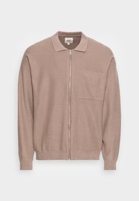 Maglione zip-up color marrone chiaro con lavorazione a maglia testurizzata, colletto, maniche lunghe, polsini a costine e una tasca sul petto, su uno sfondo bianco.