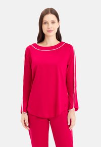 Langarm-Oberteil aus leuchtend pinkem Stoff mit rundem Ausschnitt, weißen Paspelierungen entlang der Schultern und Ärmel sowie einem geschwungenen Saum.