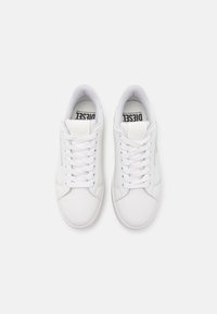 Valkea matala Diesel-kengät, joissa nauhat, nähtynä ylhäältä valkoista taustaa vasten.