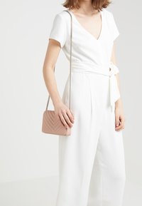 Borsa crossbody in pelle trapuntata rosa chiaro con tracolla a catena, caratterizzata da una forma rettangolare e un motivo a chevron in rilievo per aggiungere texture.