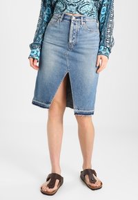 Gonna midi in denim con spacco frontale, orlo grezzo, lavaggio sbiadito e design classico a cinque tasche, abbinata a sandali marroni.