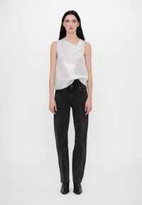 Haut sans manches en satin argenté avec un décolleté drapé, associé à un jean noir droit à taille haute et des bottines noires à talons pointus.