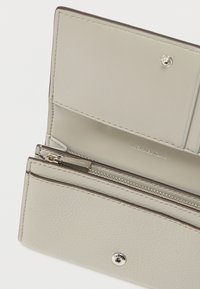 Πορτοφόλι από ανοιχτό γκρι δέρμα με φερμουάρ, θήκες για κάρτες και κλείσιμο με κουμπί, με διακριτικές ραφές και σήμανση.