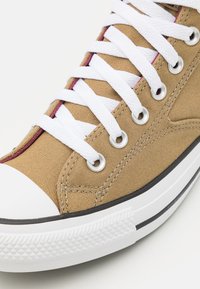 Beige kanvas hög-top sneakers med vita snören, gummitåhätta och runda ögla. Har en kontrasterande vinröd kant längs snörningsområdet.