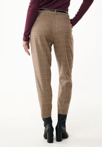 Pantaloni con un motivo a scacchi marrone con sottili accenti arancioni e crema. Design aderente, lunghezza alla caviglia, abbinati a stivaletti neri con tacco grosso.