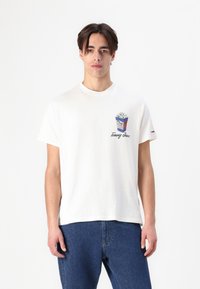 Hvit bomulls t-skjorte med et blått og hvitt popcorn-motiv og "Tommy Jeans"-logo. Korte ermer, løs passform og rund hals.
